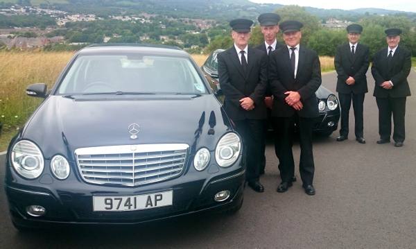 members of staff next to funeral car